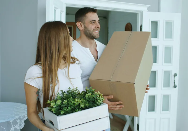 Couple carrying moving boxes into a home